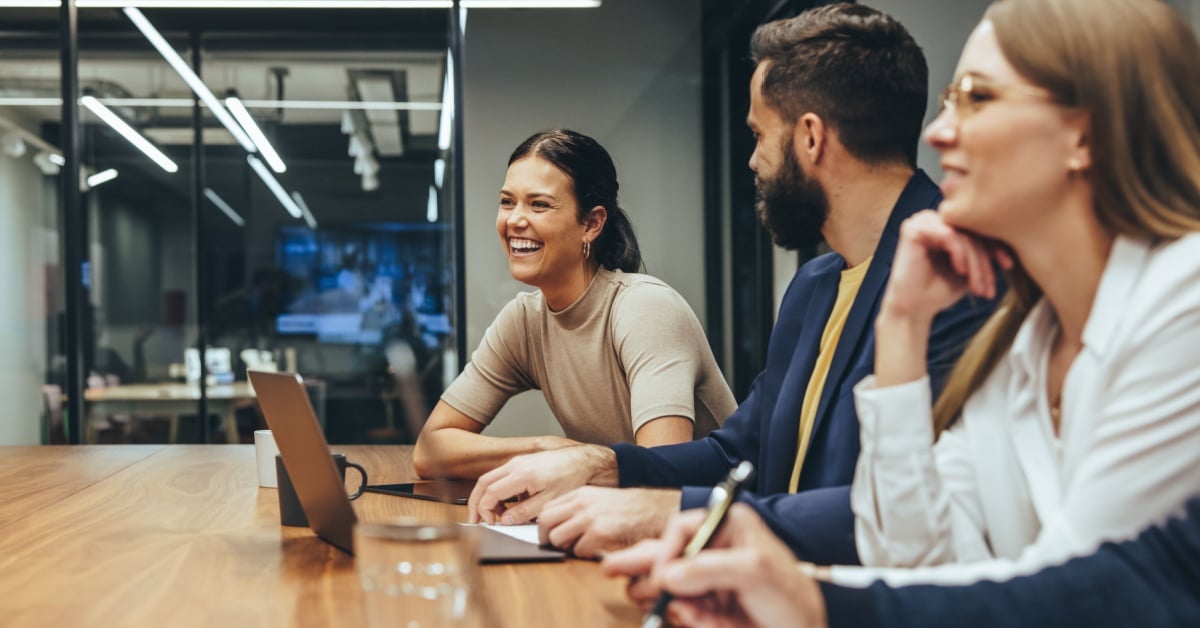 Happy businesswoman laughing while leading a meeting with her colleagues. Group of diverse businesspeople working together in a modern workplace. Business colleagues collaborating on a project.